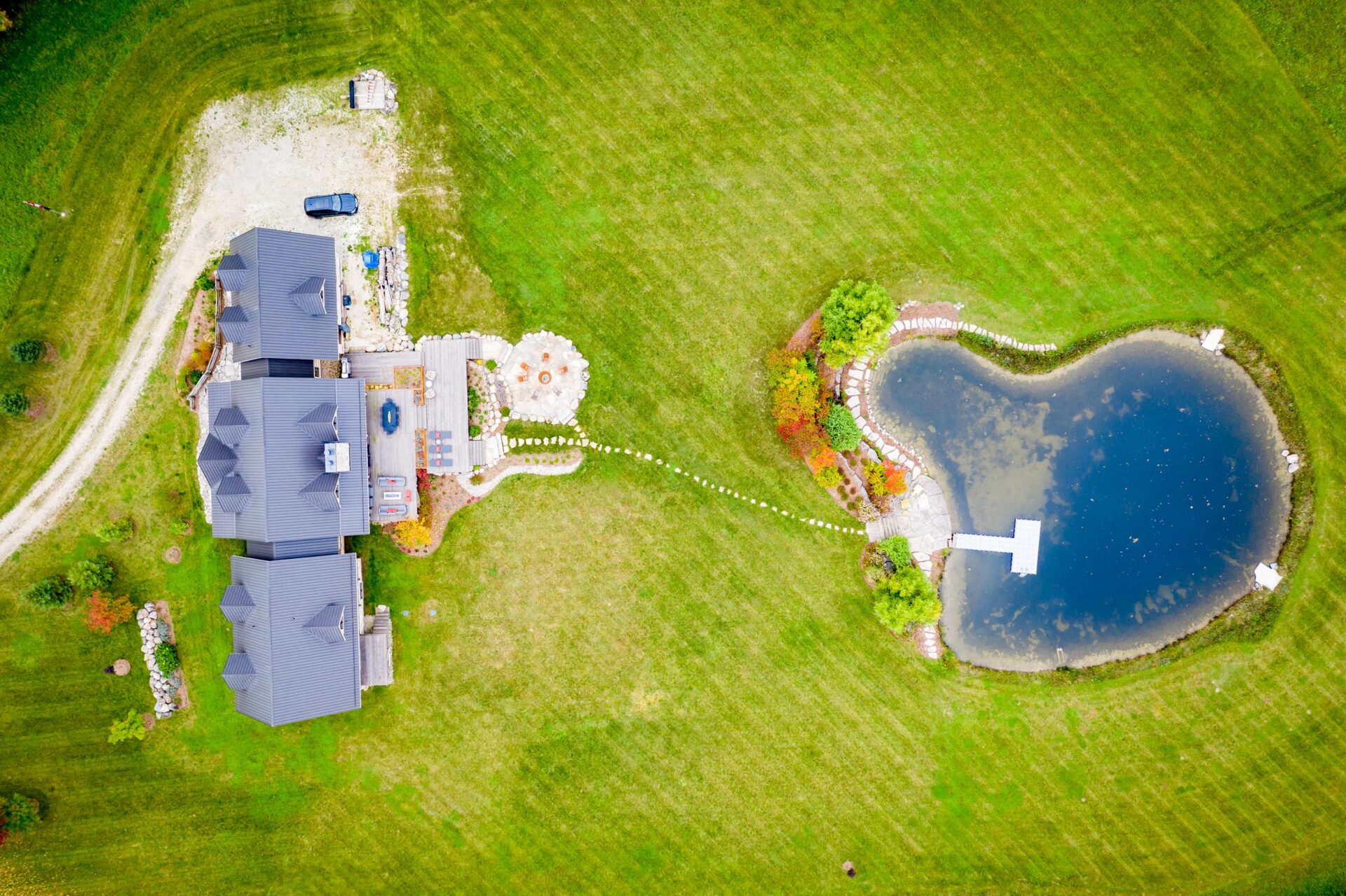 Aerial view of a property with a large house, landscaped garden, and heart-shaped pond, surrounded by expansive green lawns and a driveway.