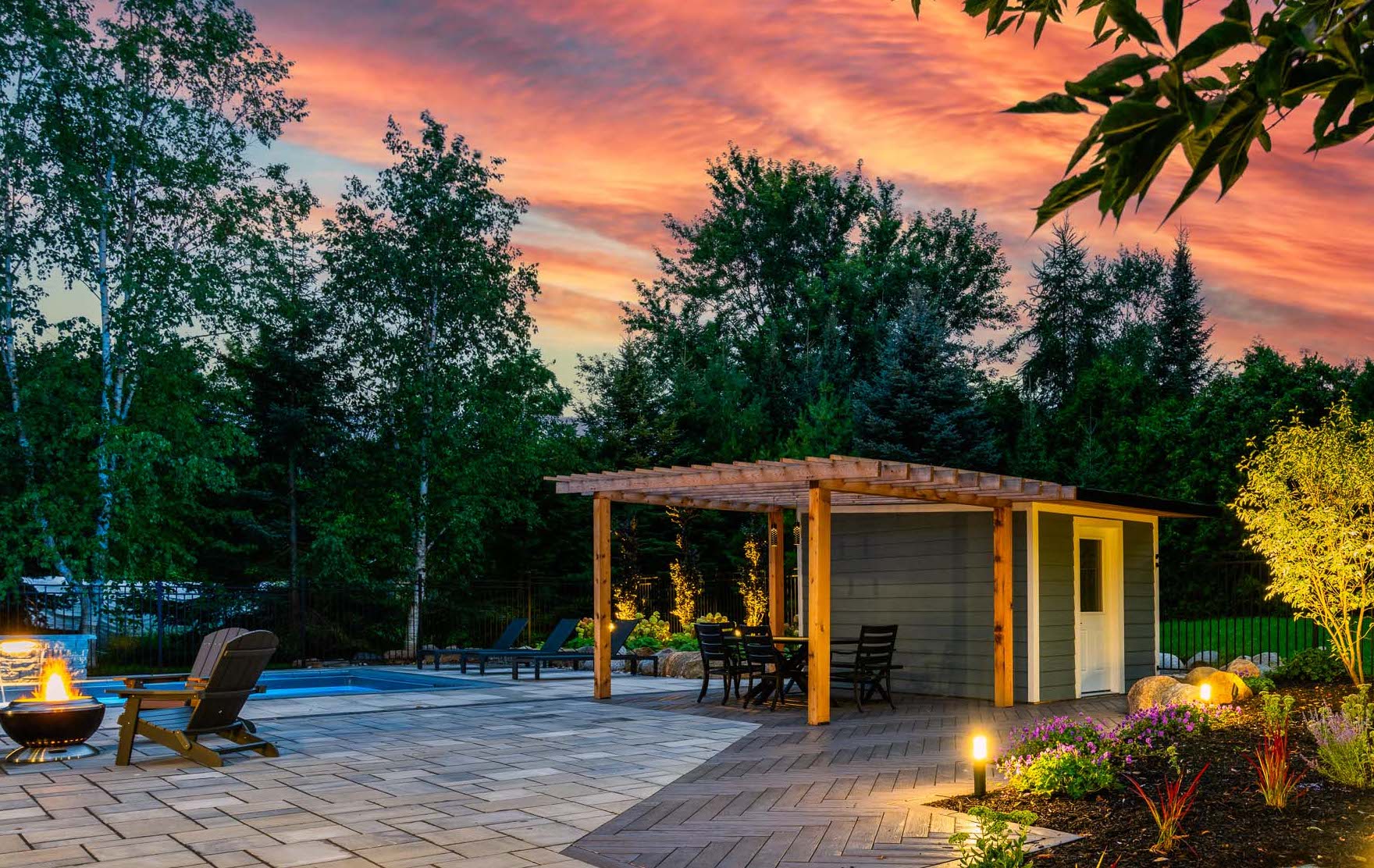 A serene backyard at dusk featuring a pergola, outdoor furniture, a fire pit, vibrant garden, and a captivating cotton-candy sky.