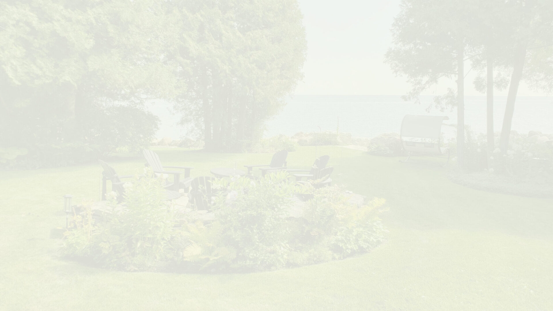 The image is overexposed, showing a serene lakeside garden with Adirondack chairs, a swing, trees, flowers, and lush green grass in bright daylight.