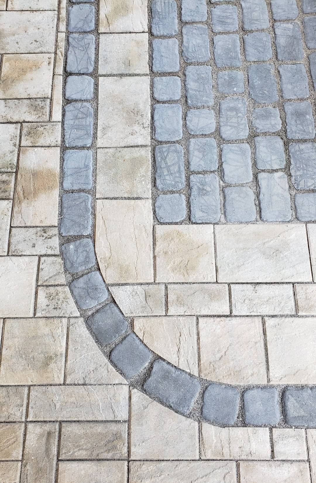 This image displays a patterned pavement with rectangular beige tiles and a curving line of square gray tiles creating a contrast in texture and color.