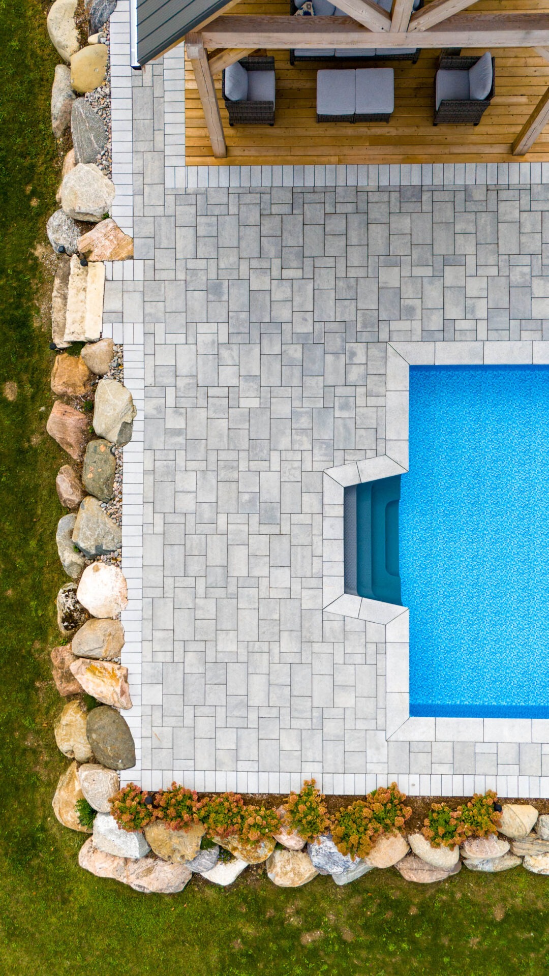 this image shows a paver patio and a boulder retaining wall with detailed cuts around the boulders and a swimming pool