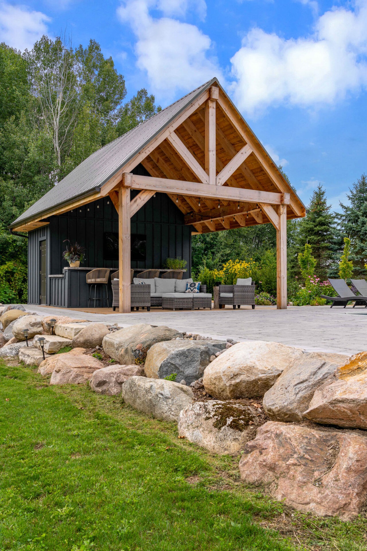 this image shows a boulder retaining wall, outdoor living room, outdoor bar, and a pool house pergola