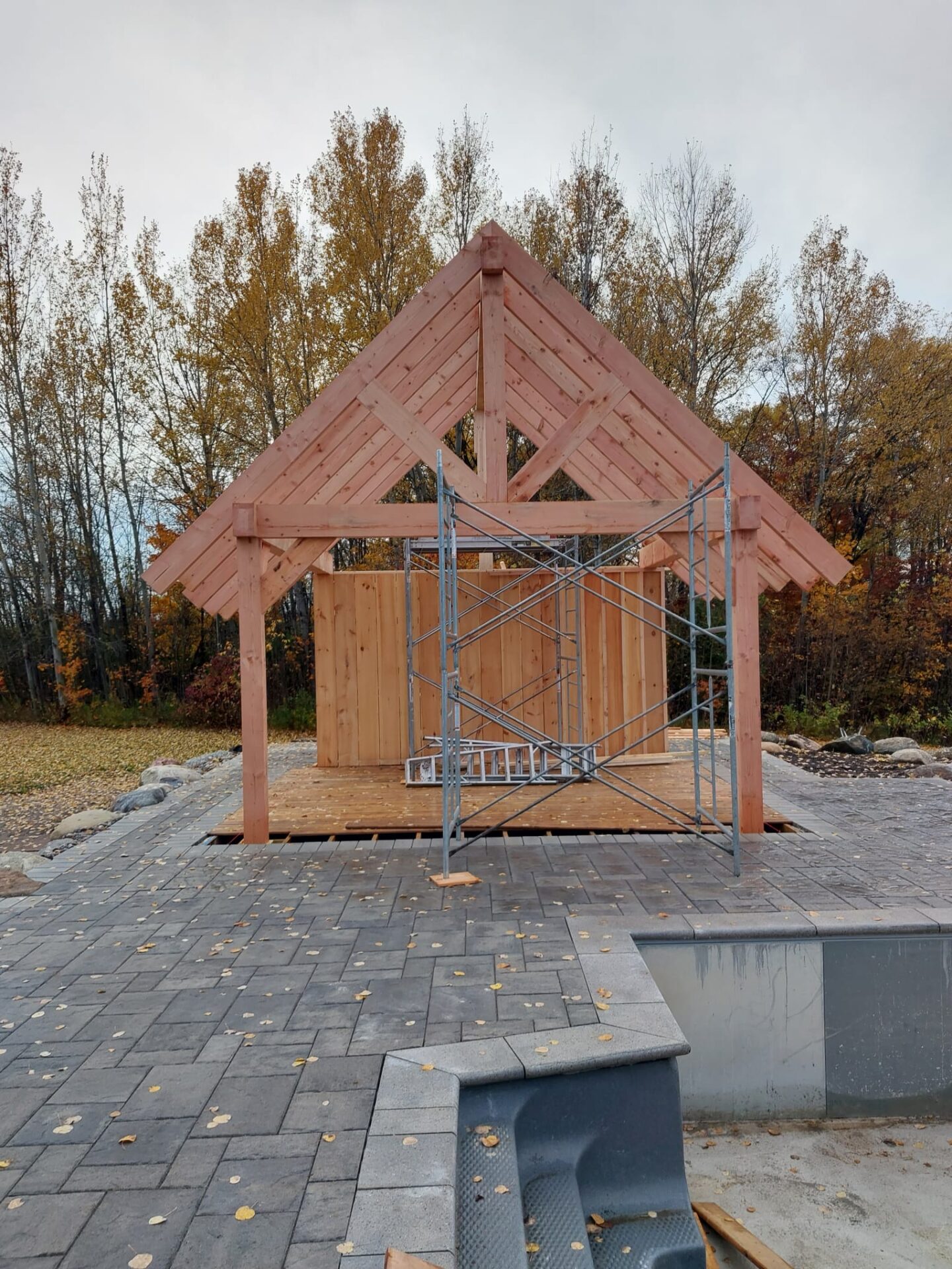 the image shows a completed pool deck and the frame of a pool house under construction