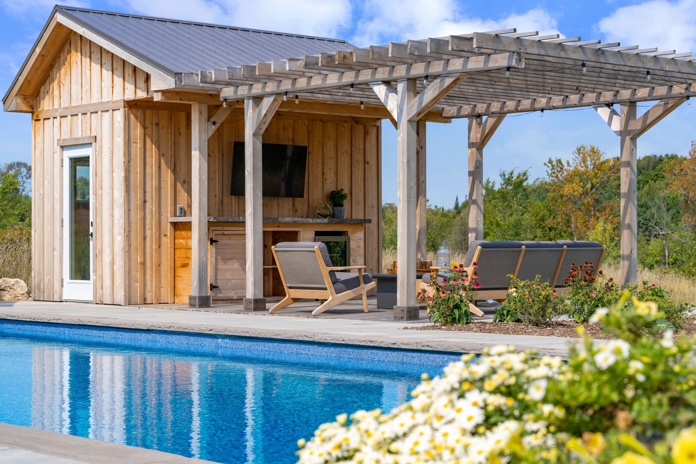 this image shows a swimming pool, pool house with sauna, outdoor living room with television and bar, pollinator gardens