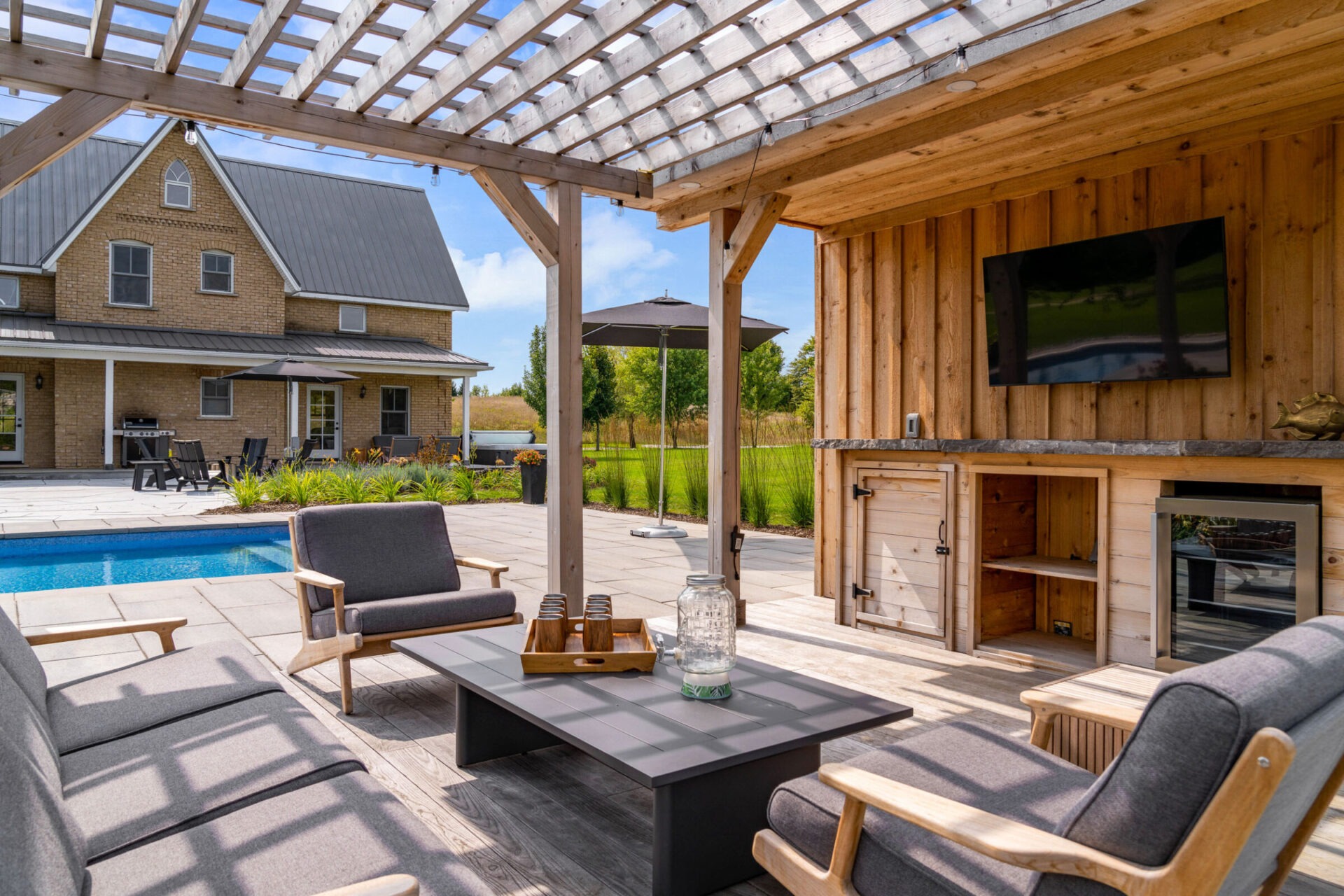 this image shows a brick farmhouse with outdoor living room, outdoor tv area, outdoor bar