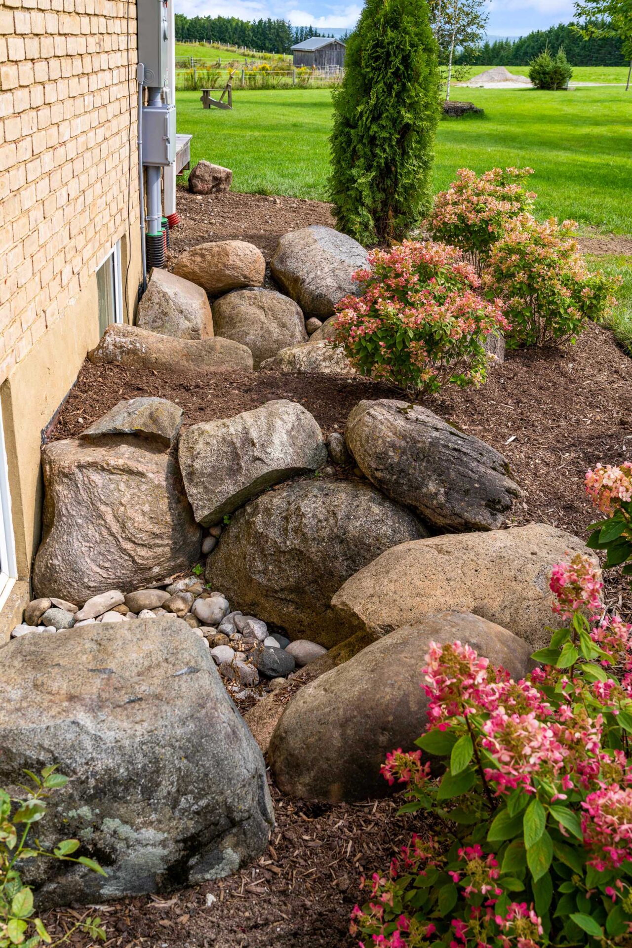 this image shows a brick farmhouse, with boulder window wells and a pollinator friendly garden