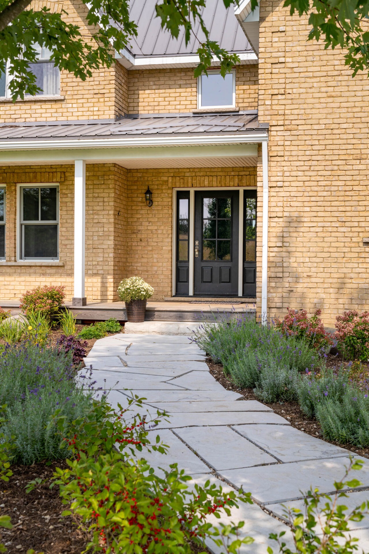 this image shows a brick farmhouse, with flagstone walkway and pollinator friendly garden.