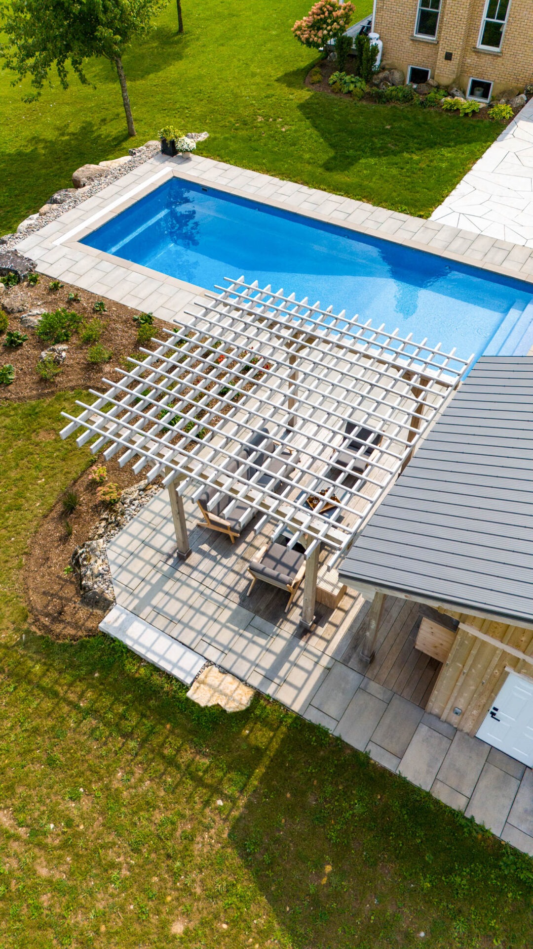 this image shows a swimming pool, pergola, pool house with sauna, outdoor living room with television and bar, pollinator gardens