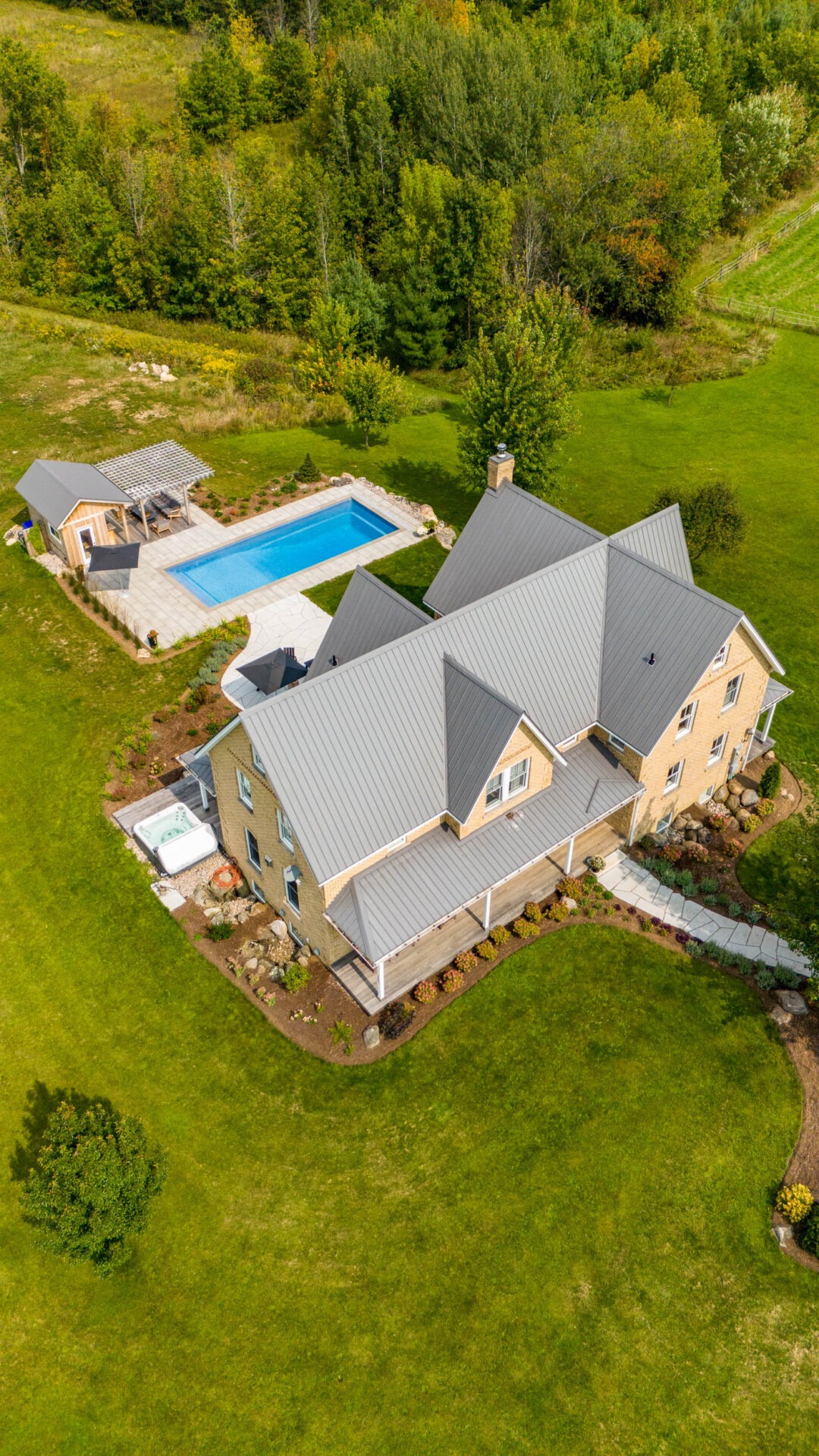 this image shows a brick farmhouse, swimming pool, pergola, pool house with sauna, outdoor living room with television and bar, pollinator gardens