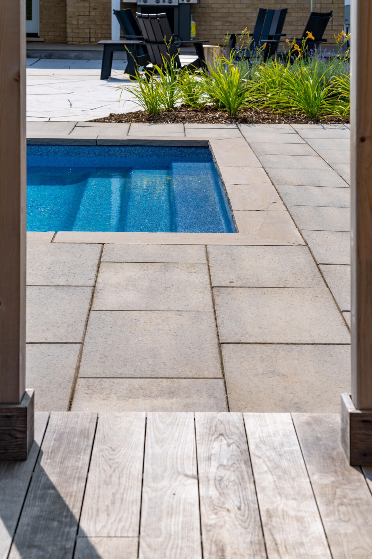 this image shows a swimming pool and transition from thermory decking to paver patio to swimming pool