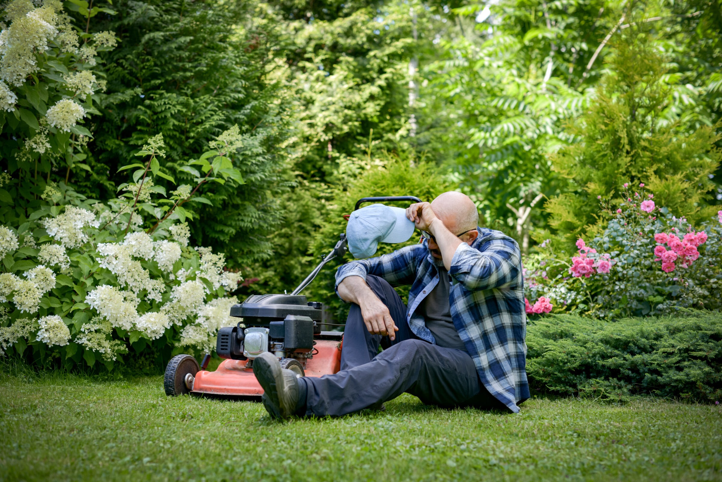 tired mature adult man mows the grass in the garden with a lawn mower