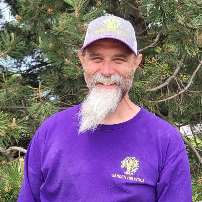 a smiling person with a beard wearing a purple uniform shirt