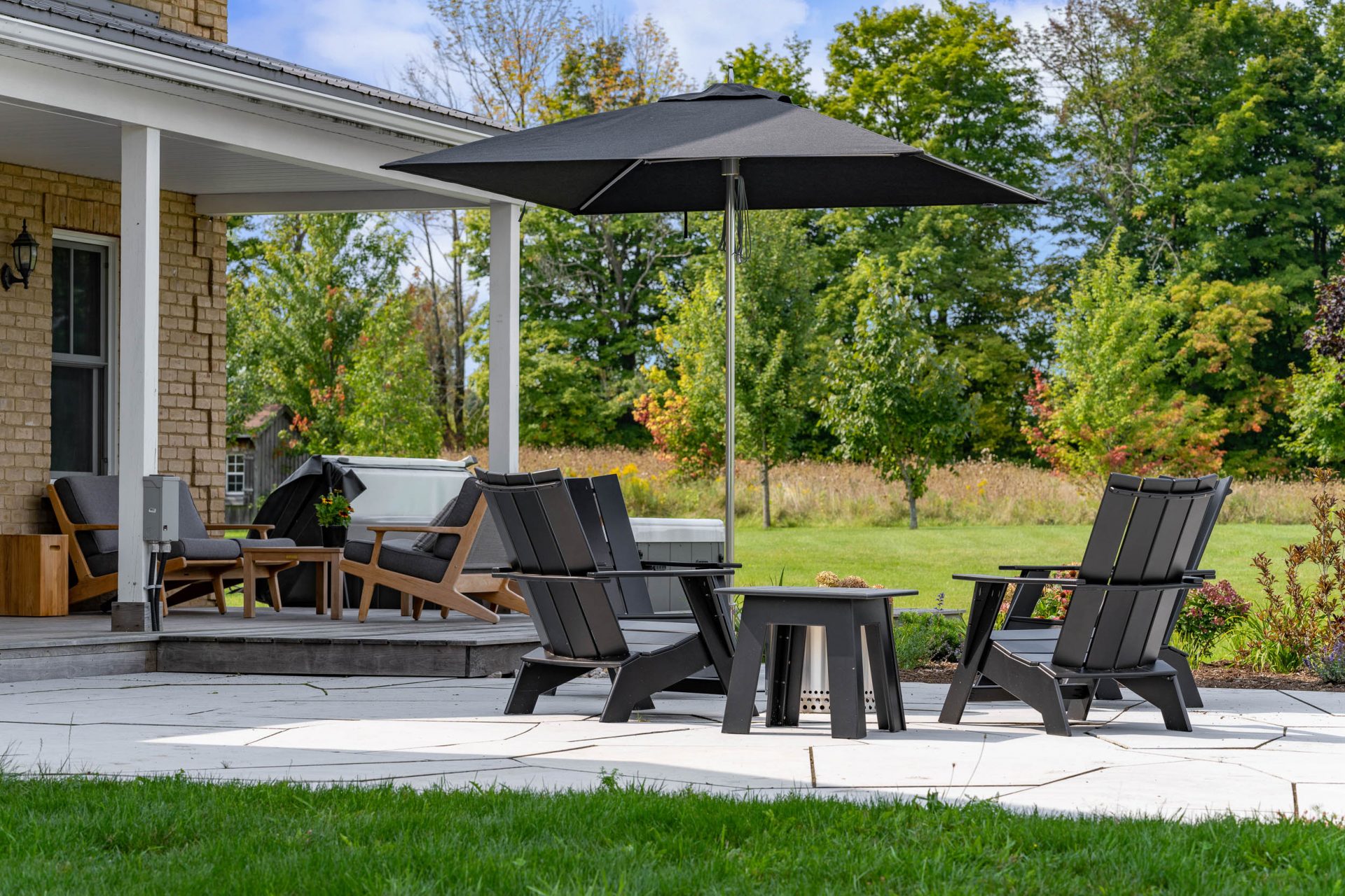 Backyard patio with Adirondack chairs and umbrella near a modern home.